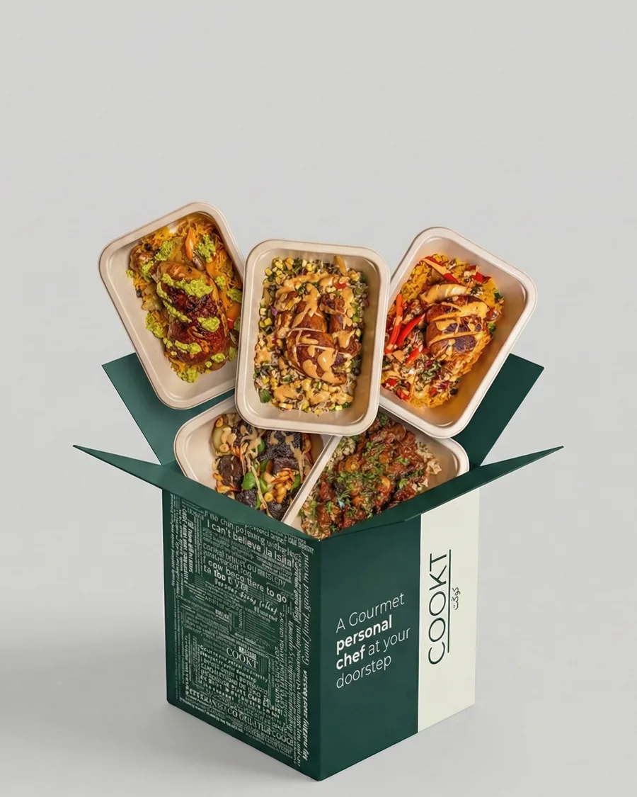 An open COOKT box with sealed meal trays lifting out of it