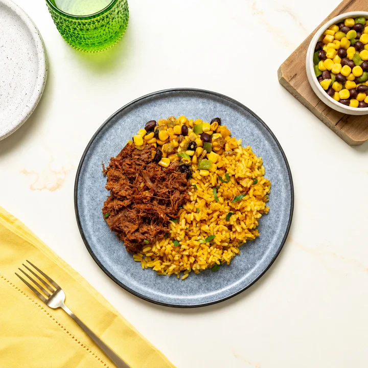 Plated chef-cooked halal meal with seasoned shredded beef, saffron yellow rice, and corn and black bean salsa