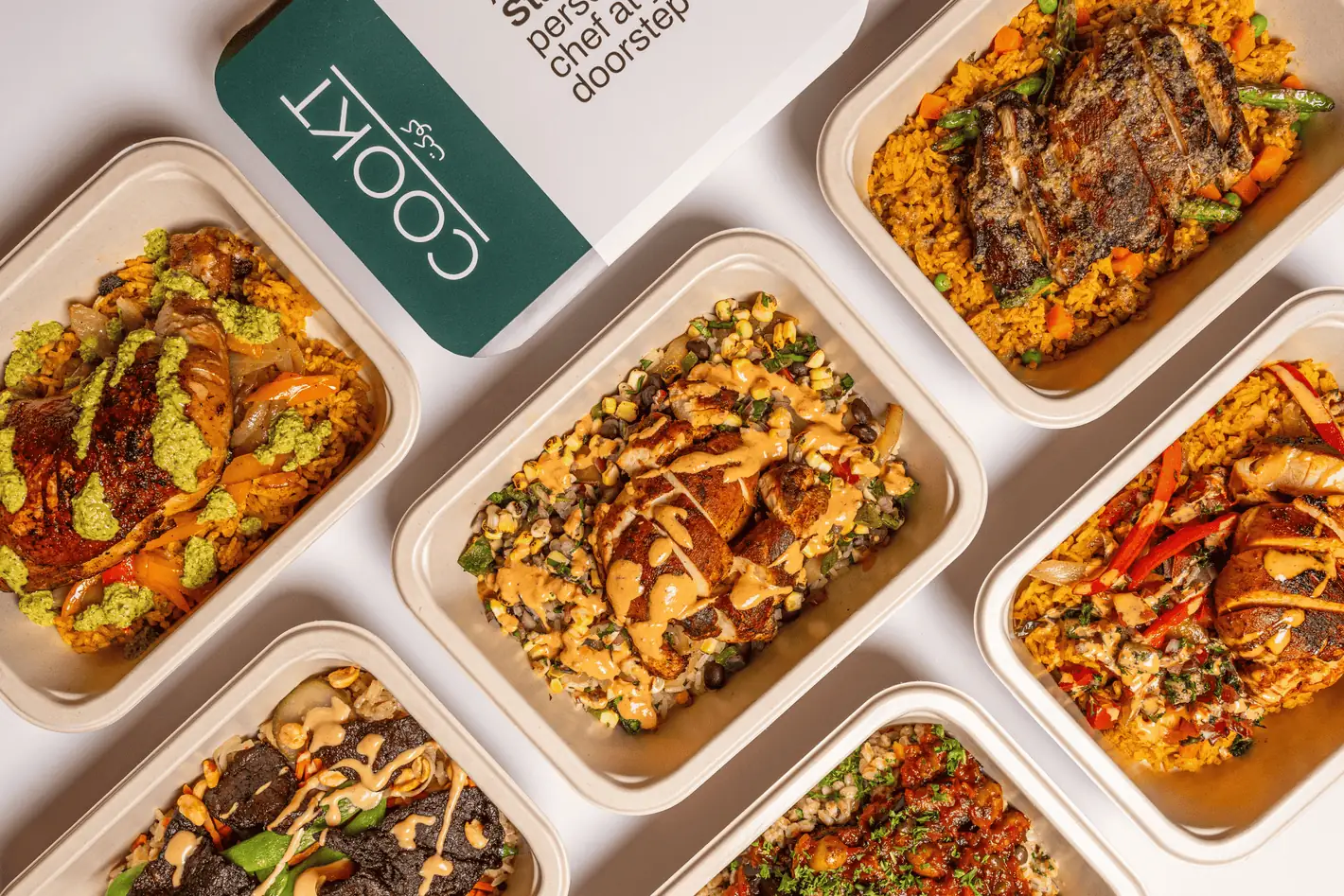 An overhead spread of COOKT chef-cooked halal meals in sealed trays beside a COOKT delivery box