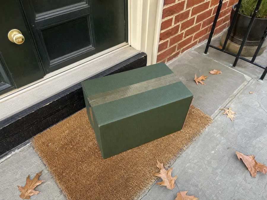 An insulated meal delivery box on the doormat outside the front door of a brick townhouse